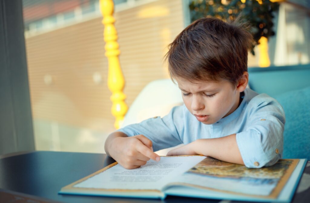 A child struggles to read a book due to their blurry vision.