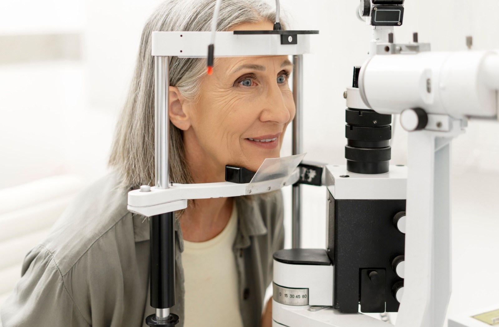 Older woman undergoing an eye exam with a slit lamp machine during a comprehensive eye exam at an optometrist’s office.