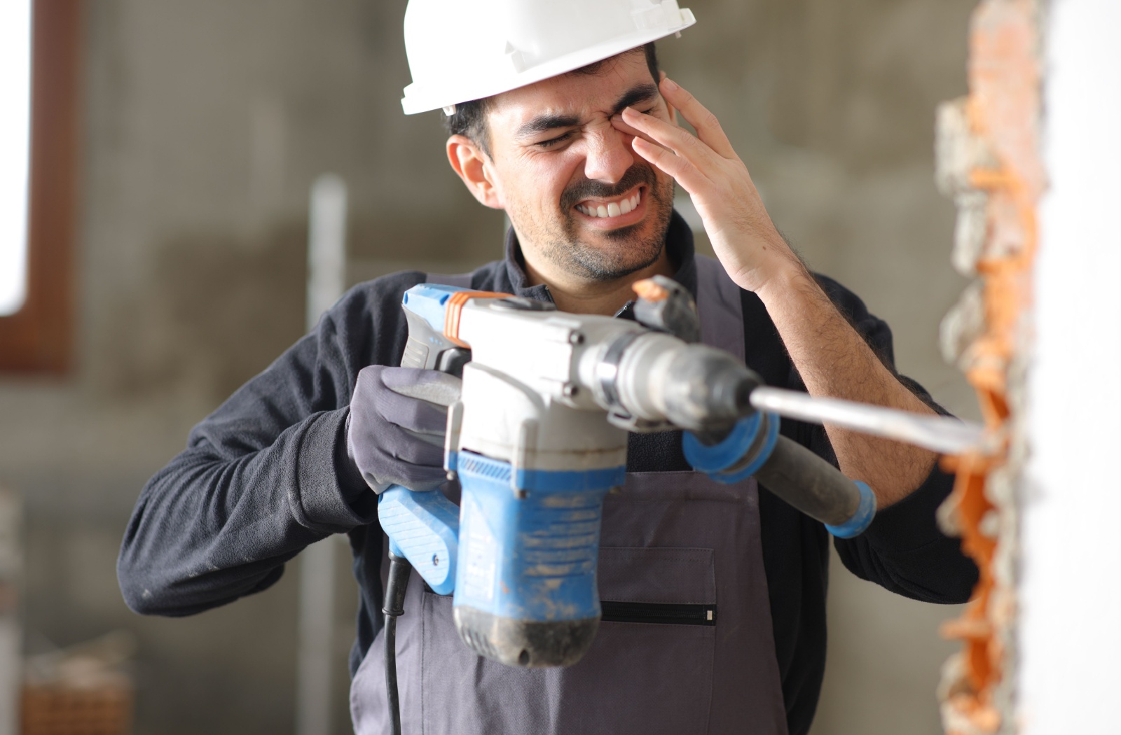 Construction worker holding left eye in pain after brick wall he was drilling shattered.